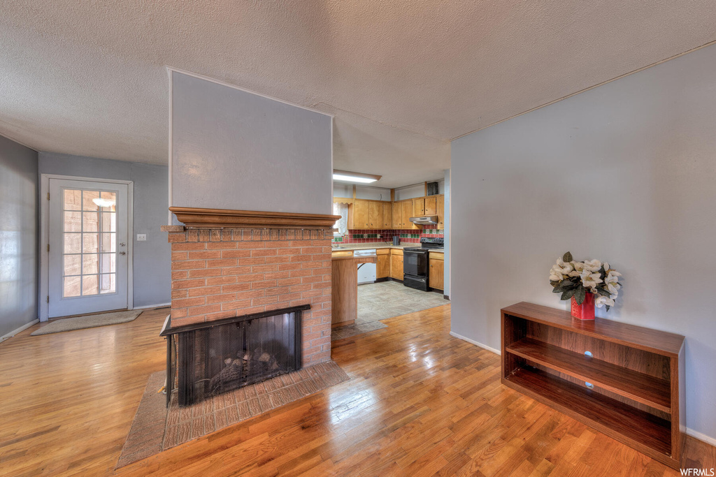 Living room with a brick fireplace, a textured ceiling, and light hardwood / wood-style flooring