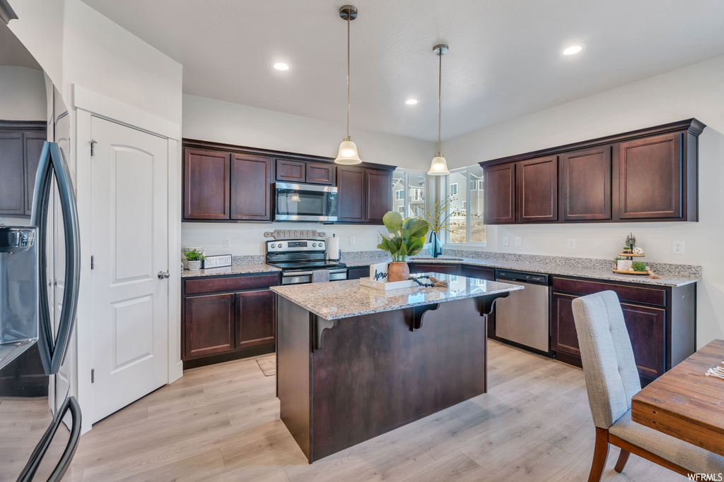 Kitchen featuring appliances with stainless steel finishes, pendant lighting, a center island, light stone countertops, and light wood-type flooring