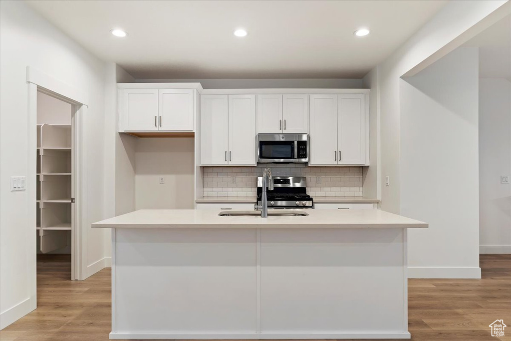 Kitchen with white cabinetry, appliances with stainless steel finishes, a kitchen island with sink, and light hardwood / wood-style flooring