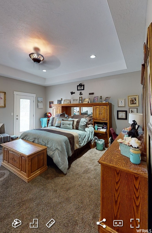 Bedroom with a tray ceiling, ceiling fan, and dark colored carpet