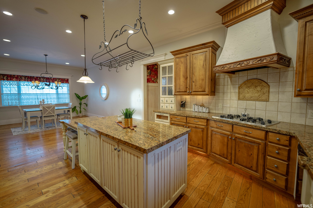 Kitchen with light hardwood / wood-style flooring, custom exhaust hood, a center island, and backsplash