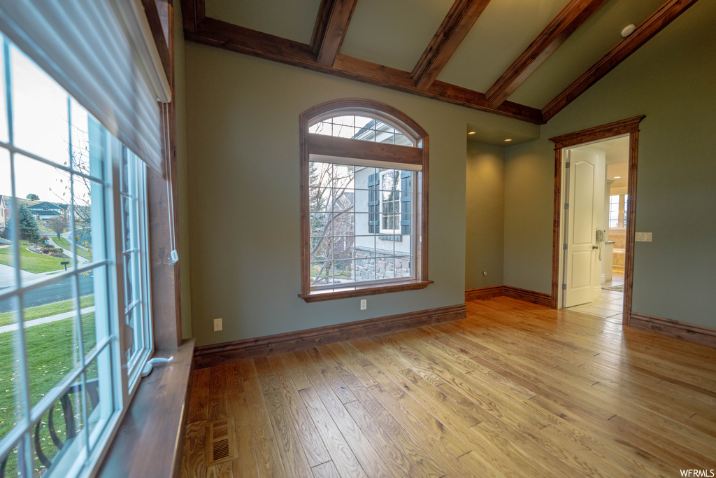 Empty room featuring vaulted ceiling with beams, plenty of natural light, and light hardwood / wood-style floors