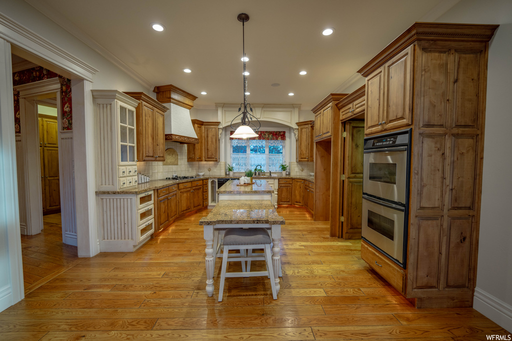 Kitchen featuring premium range hood, light hardwood / wood-style floors, stainless steel appliances, tasteful backsplash, and a kitchen island