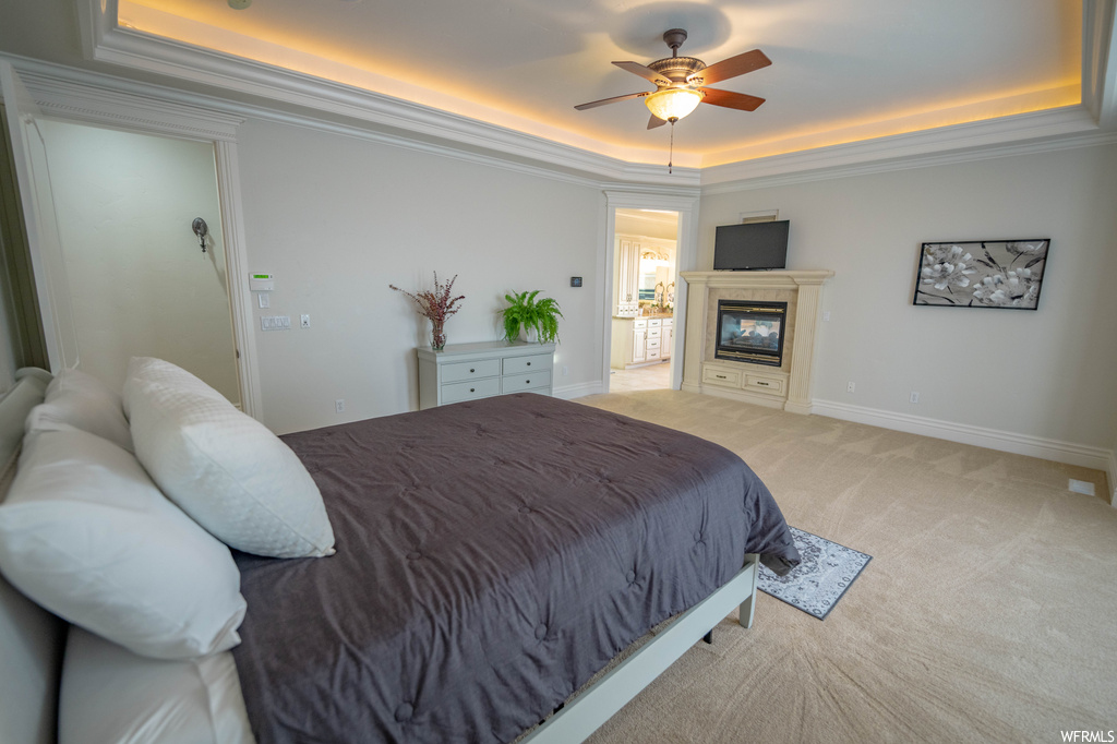 Carpeted bedroom with ornamental molding, a tray ceiling, and ceiling fan