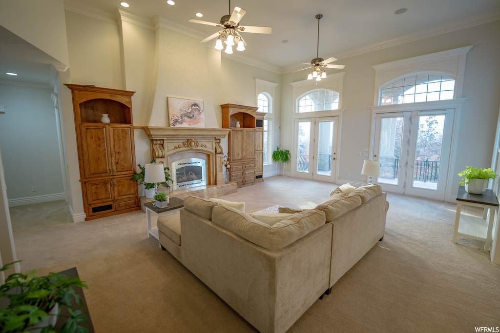 Carpeted living room featuring french doors, ceiling fan, ornamental molding, and a high ceiling