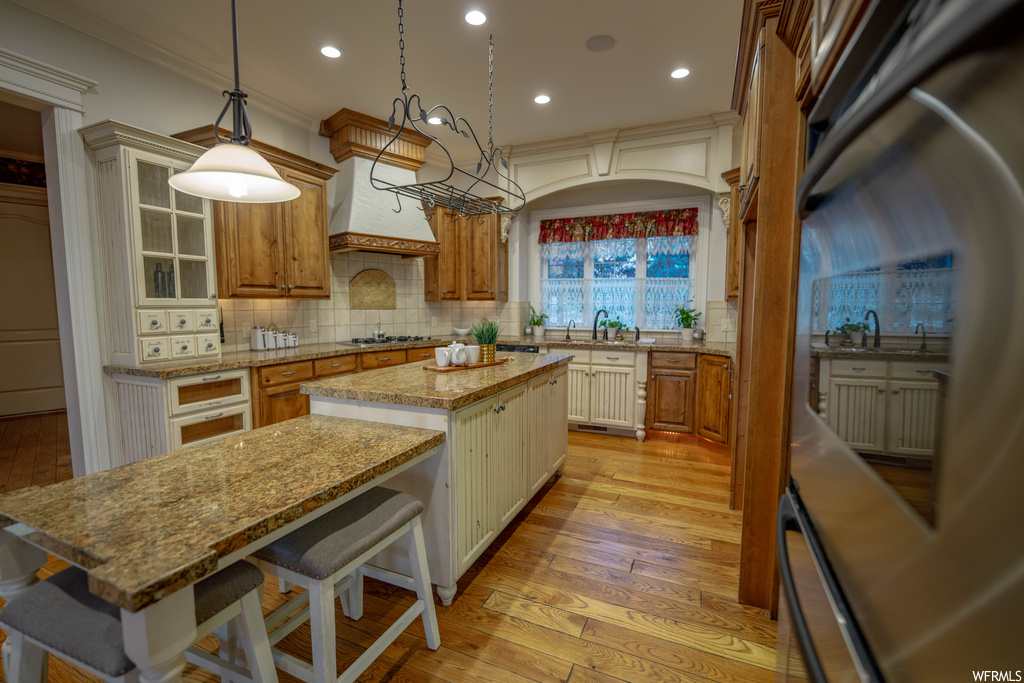 Kitchen with tasteful backsplash, light stone counters, decorative light fixtures, light wood-type flooring, and a kitchen island