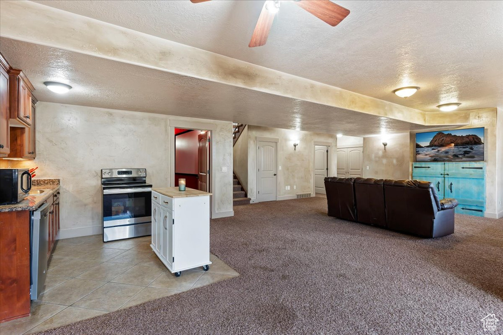 Kitchen with light colored carpet, ceiling fan, stainless steel appliances, and a textured ceiling