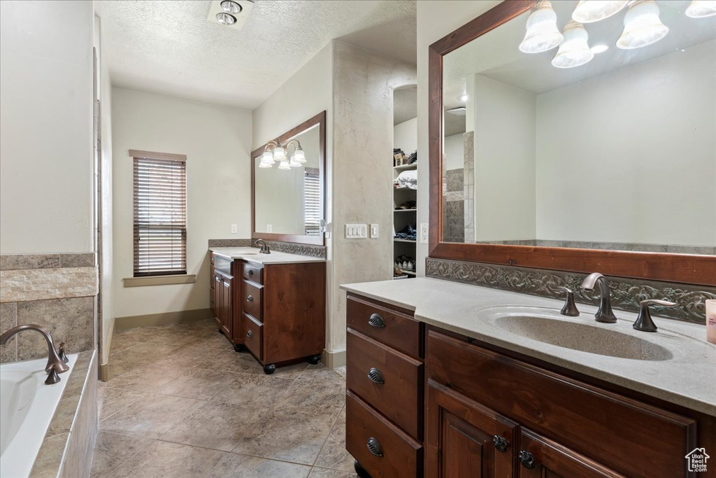 Bathroom featuring tiled bath, vanity, tile flooring, a notable chandelier, and a textured ceiling