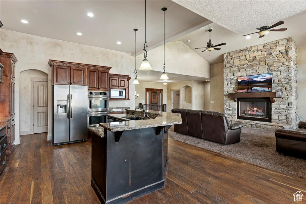 Kitchen featuring a fireplace, dark hardwood / wood-style floors, stainless steel appliances, a kitchen bar, and ceiling fan