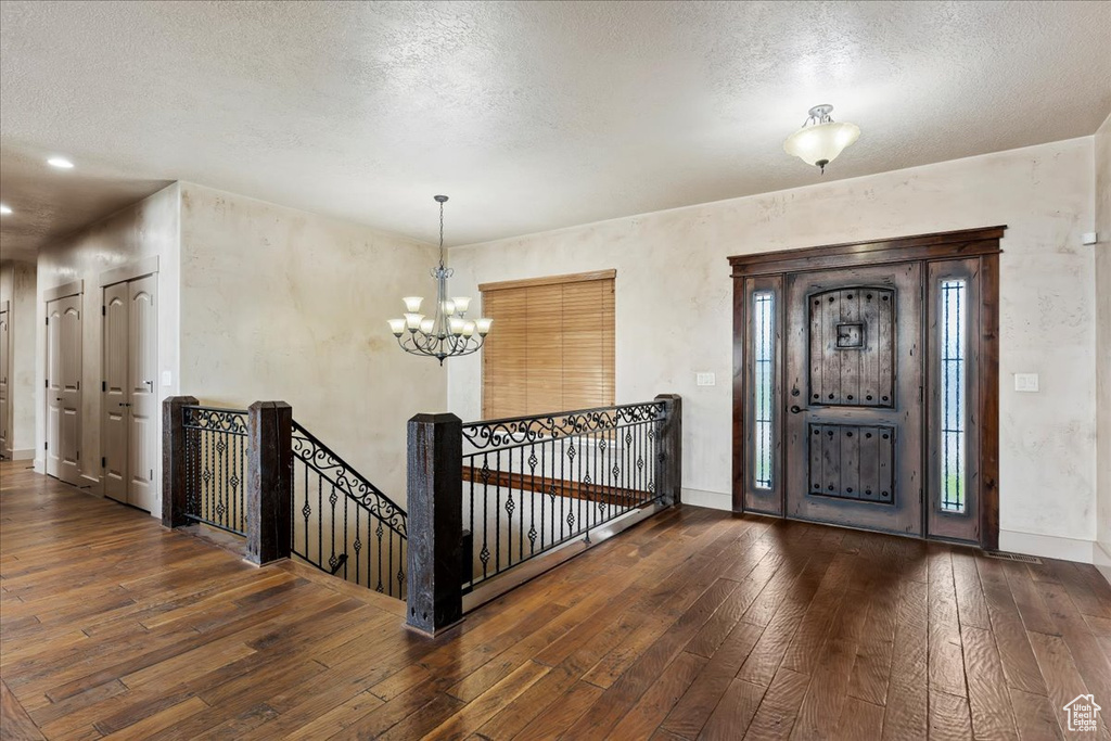 Foyer entrance with a textured ceiling, an inviting chandelier, and dark wood-type flooring
