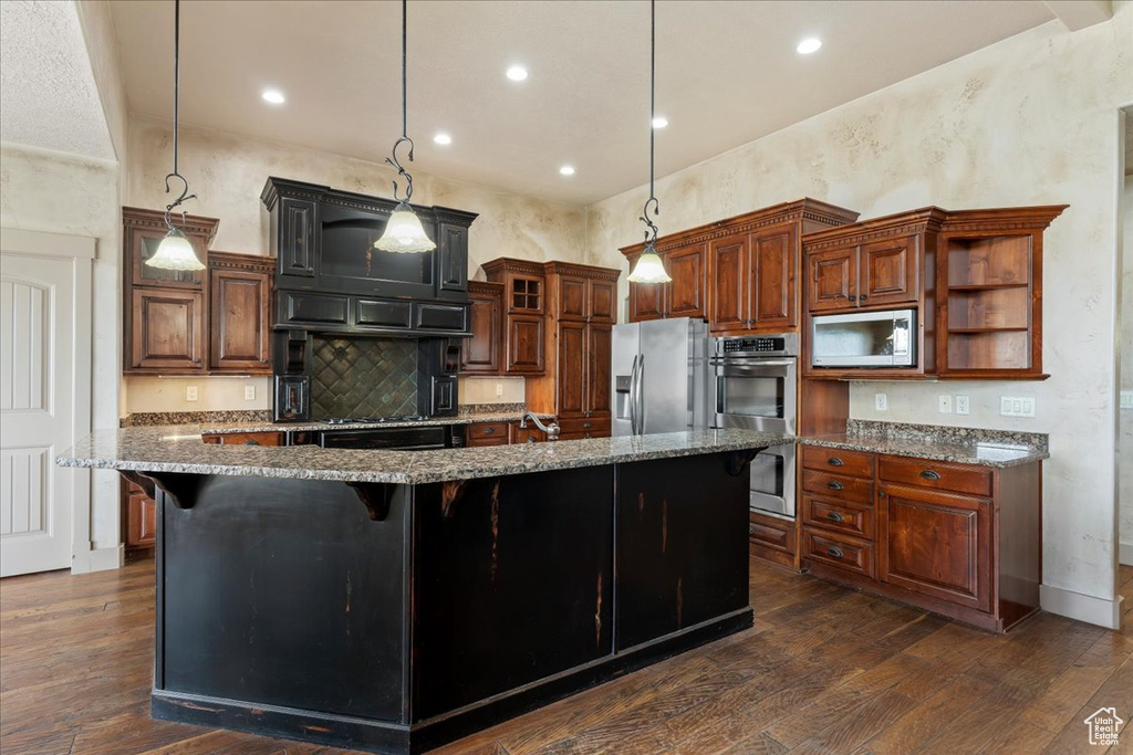 Kitchen with decorative light fixtures, a spacious island, dark hardwood / wood-style floors, appliances with stainless steel finishes, and a kitchen bar