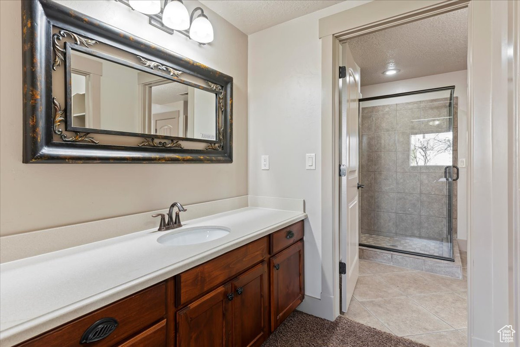 Bathroom featuring a shower with shower door, oversized vanity, a textured ceiling, and tile flooring