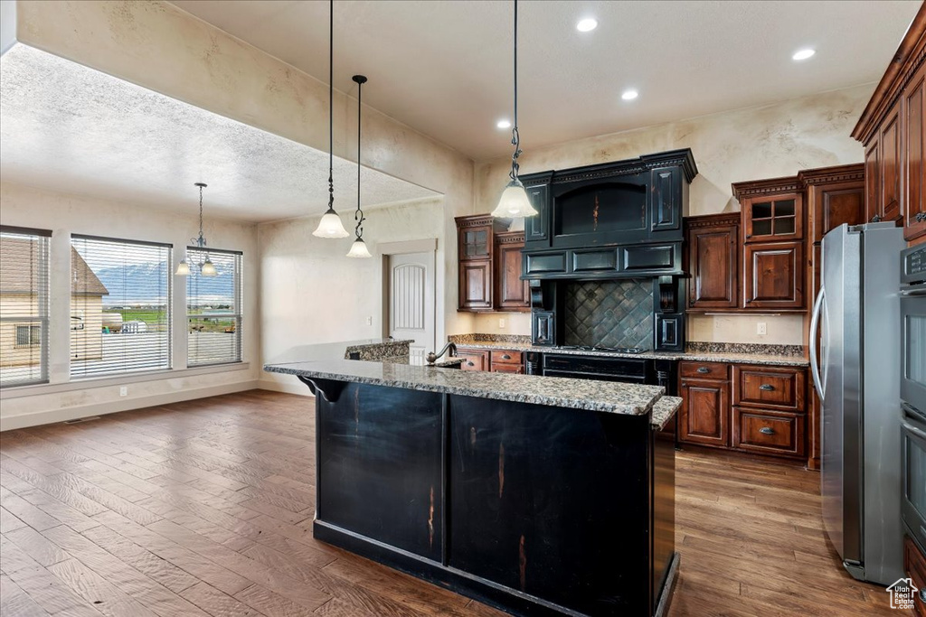 Kitchen featuring light stone counters, a kitchen bar, stainless steel refrigerator, decorative light fixtures, and dark hardwood / wood-style flooring
