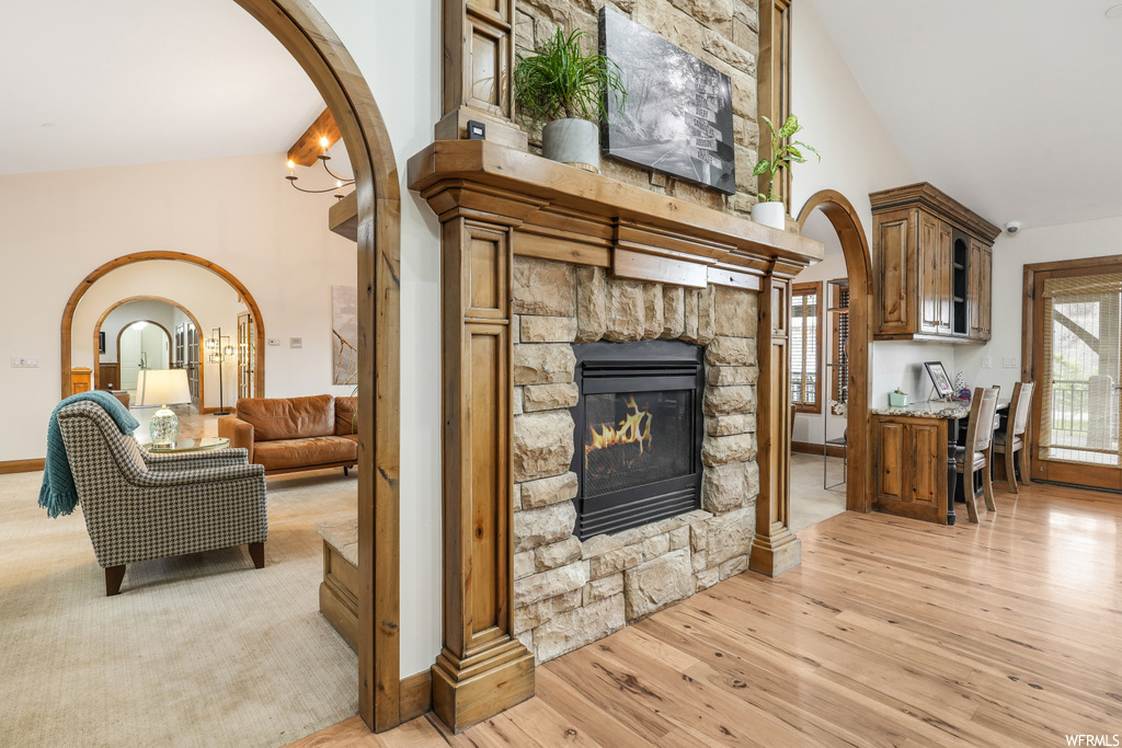 Living room featuring light wood-type flooring, a stone fireplace, and high vaulted ceiling