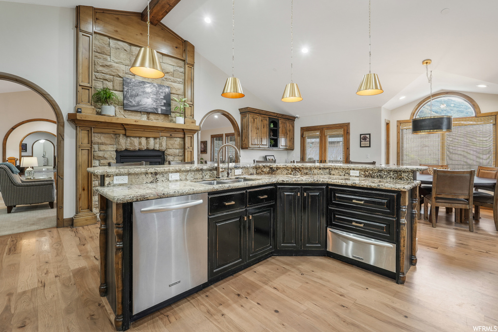 Kitchen featuring sink, light stone counters, stainless steel dishwasher, light wood-type flooring, and decorative light fixtures