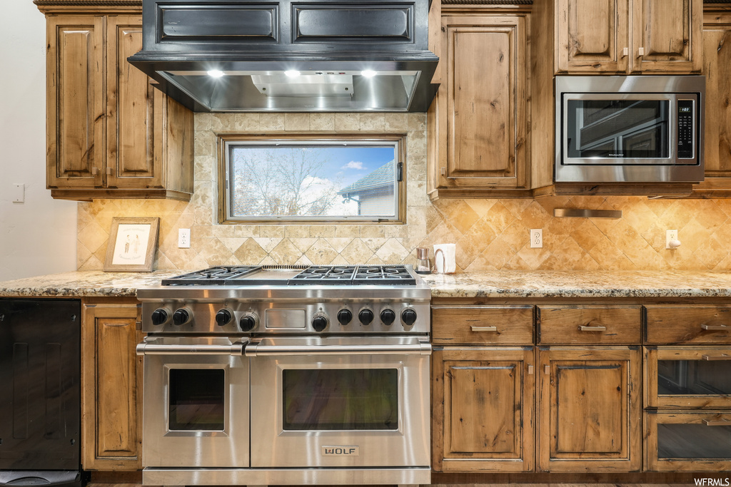 Kitchen with tasteful backsplash, wall chimney range hood, light stone countertops, and stainless steel appliances