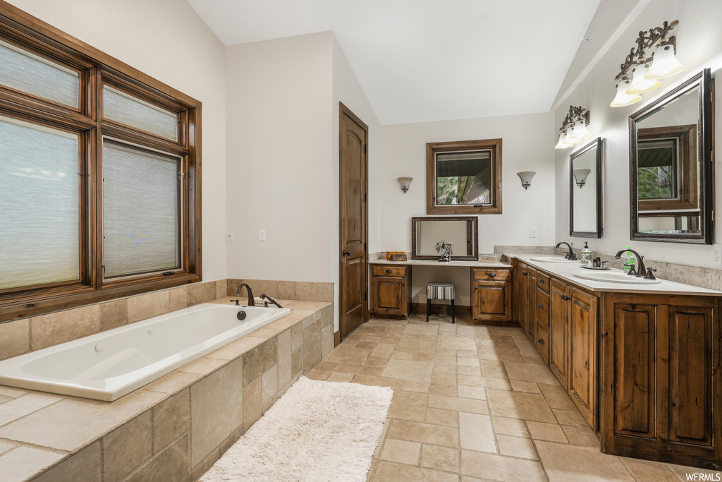 Bathroom featuring vaulted ceiling, oversized vanity, dual sinks, a relaxing tiled bath, and tile floors