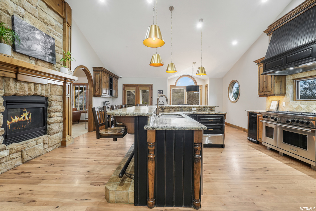 Kitchen featuring sink, a kitchen island with sink, double oven range, light hardwood / wood-style floors, and a stone fireplace