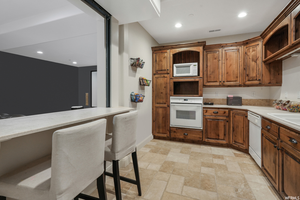 Kitchen with white appliances, a breakfast bar area, and light tile flooring