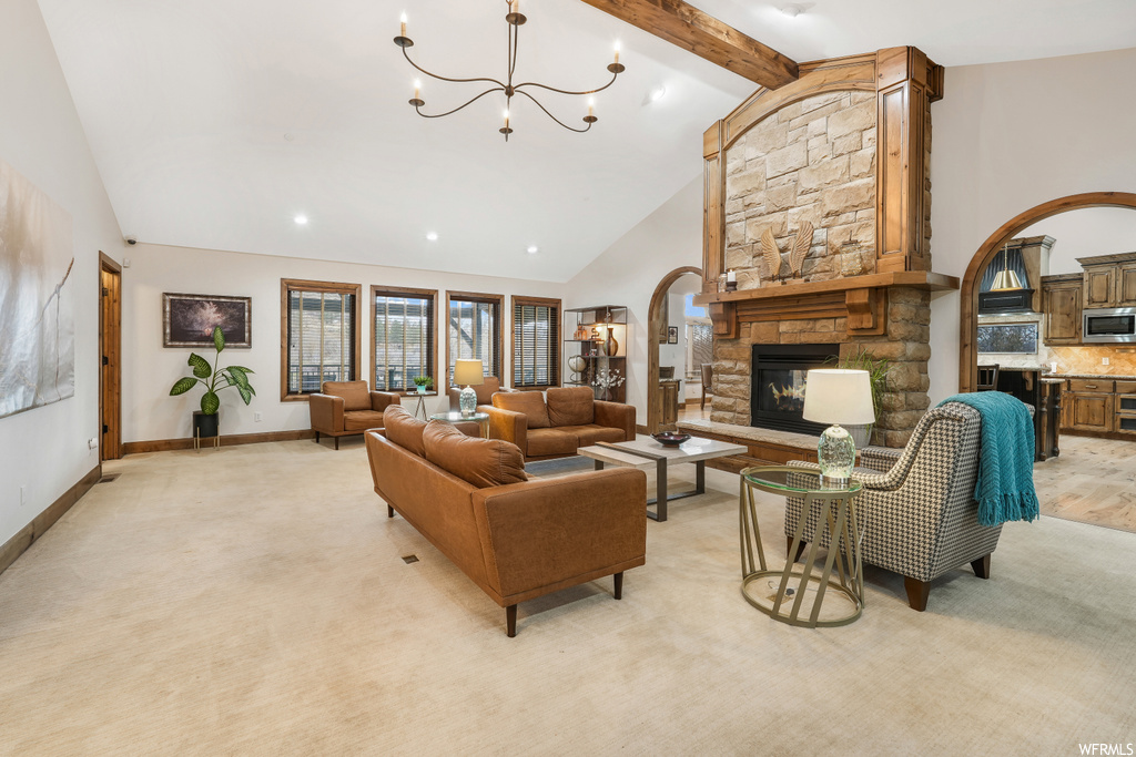 Carpeted living room featuring beamed ceiling, high vaulted ceiling, a stone fireplace, and a notable chandelier