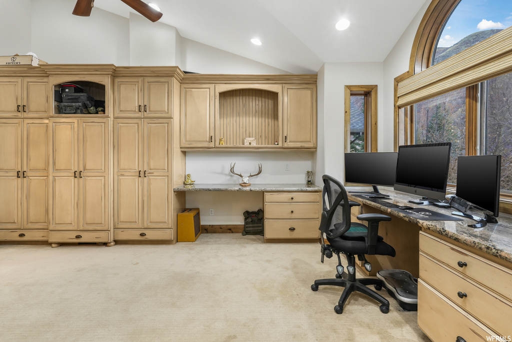 Carpeted office space with ceiling fan, built in desk, and vaulted ceiling
