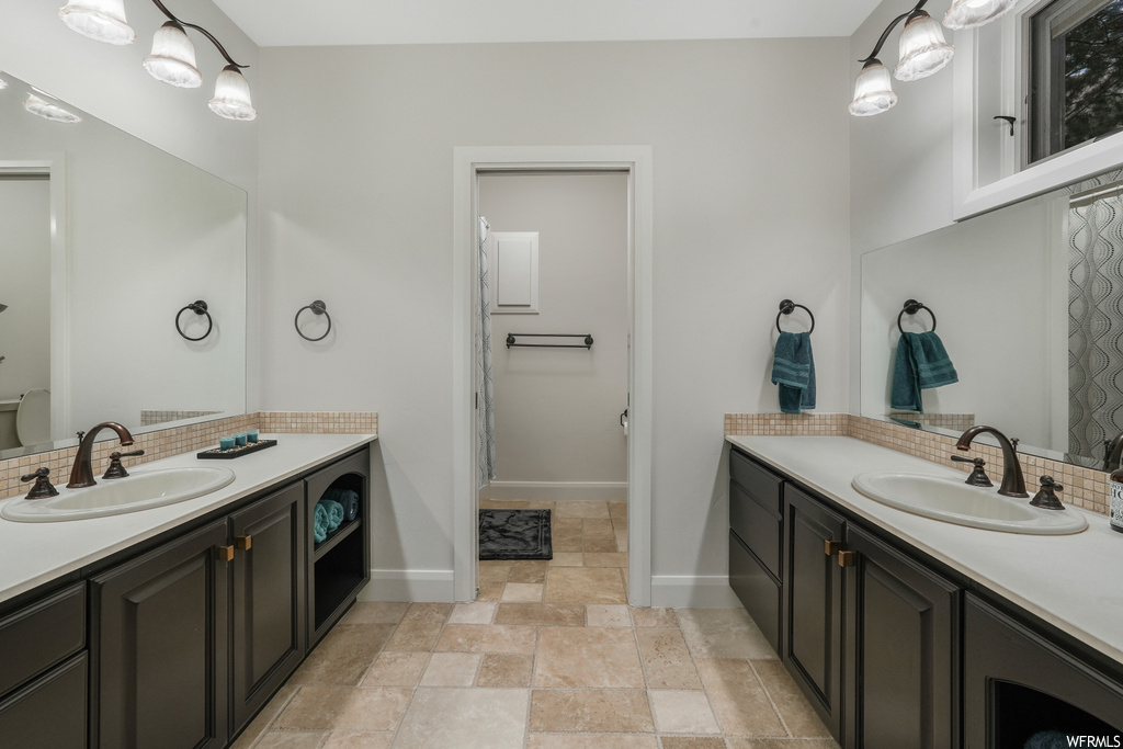 Bathroom with double sink, tile floors, backsplash, and vanity with extensive cabinet space