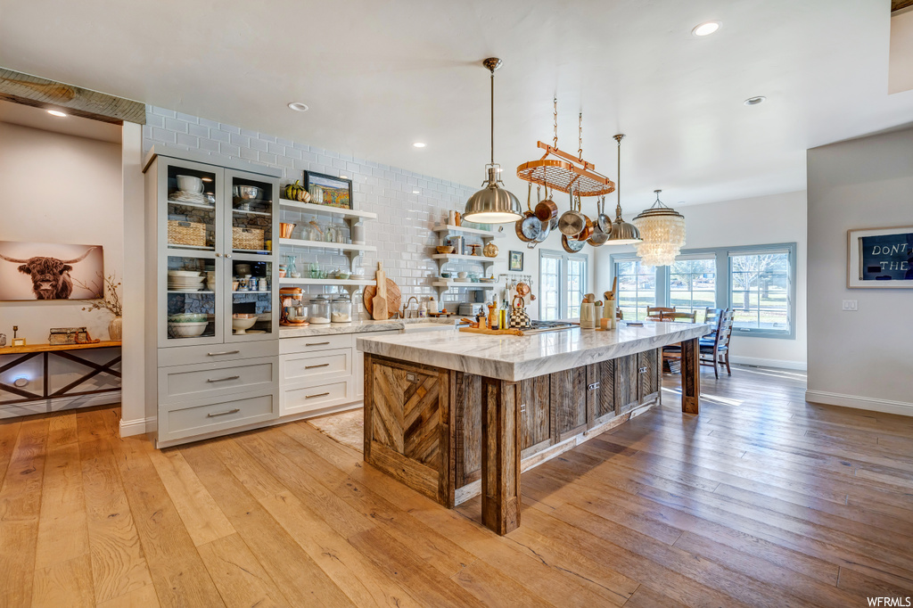 Kitchen featuring a chandelier, a kitchen island with sink, hanging light fixtures, light hardwood / wood-style floors, and tasteful backsplash