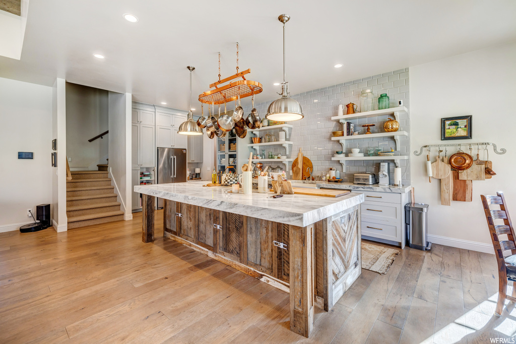 Kitchen with light hardwood / wood-style floors, pendant lighting, a kitchen island with sink, tasteful backsplash, and white cabinets