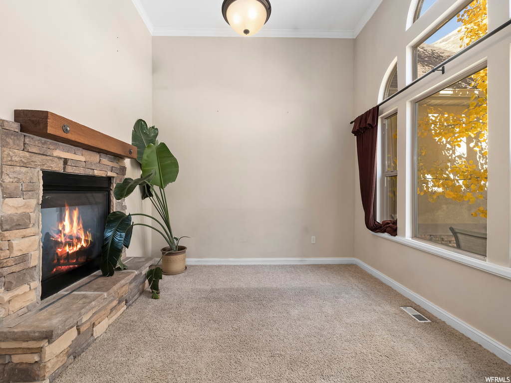 Unfurnished living room featuring ornamental molding, light colored carpet, and a fireplace