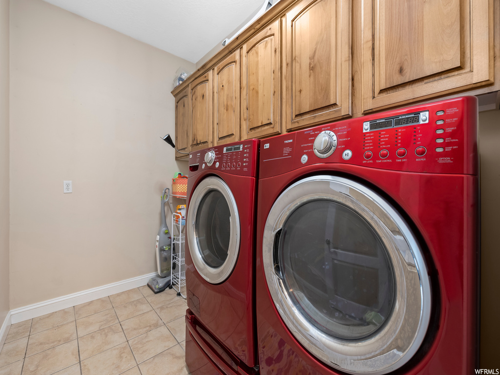 Laundry area featuring light tile floors, separate washer and dryer, and cabinets