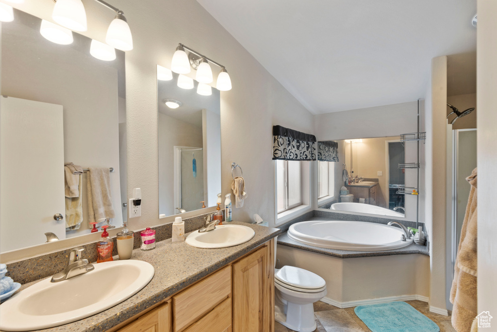 Bathroom with double sink vanity, lofted ceiling, toilet, tile floors, and a bath to relax in