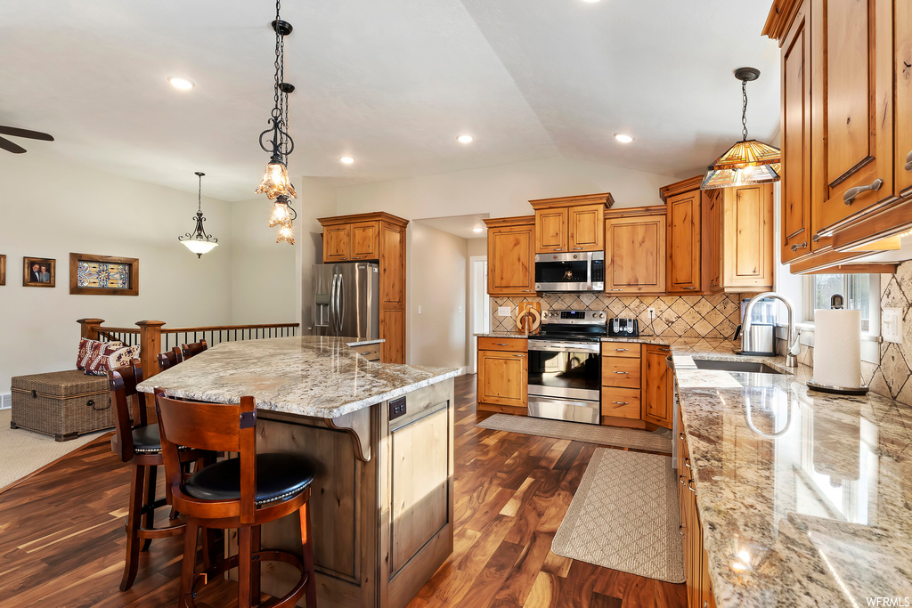 Kitchen with hanging light fixtures, sink, light stone countertops, stainless steel appliances, and ceiling fan