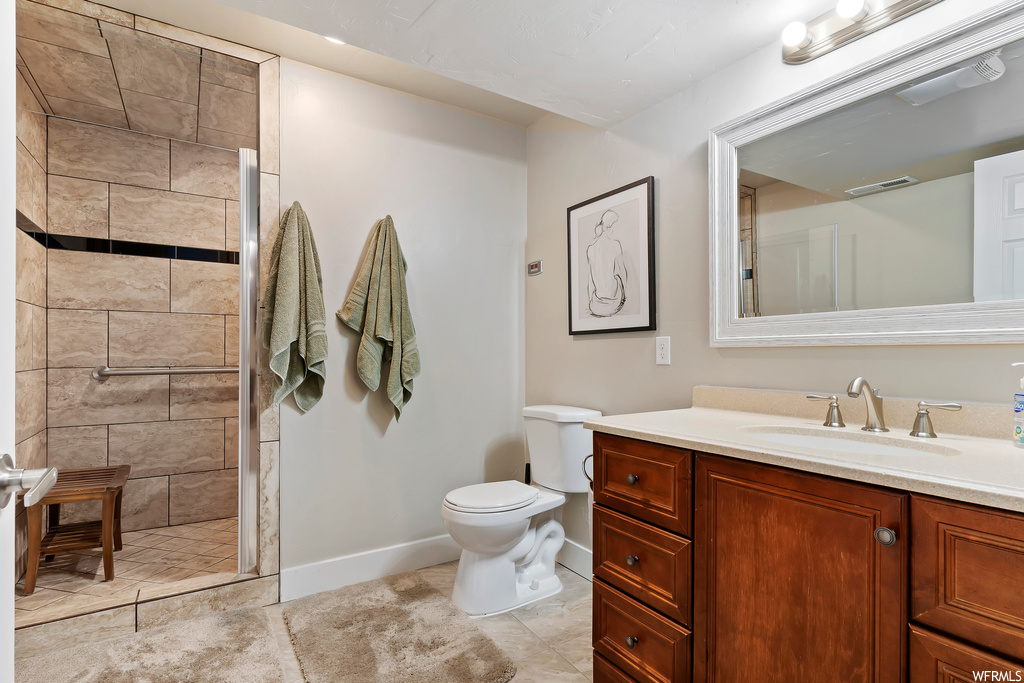 Bathroom featuring toilet, tile floors, tiled shower, and vanity