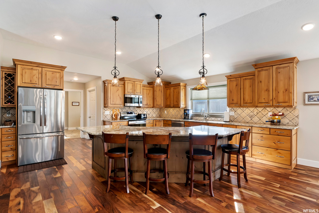 Kitchen featuring dark wood-type flooring, tasteful backsplash, stainless steel appliances, decorative light fixtures, and a kitchen island