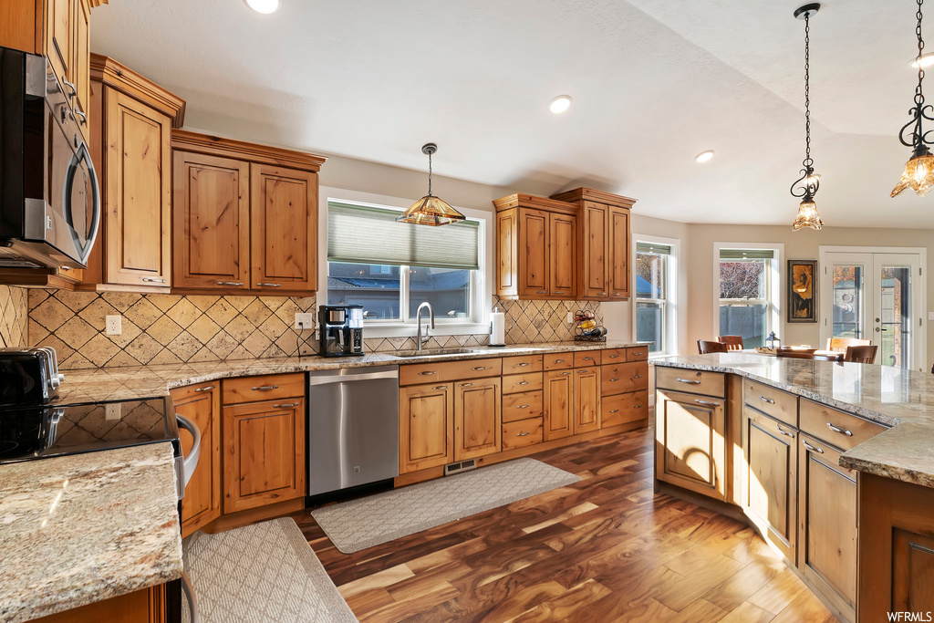 Kitchen with backsplash, pendant lighting, stainless steel appliances, and light hardwood / wood-style flooring