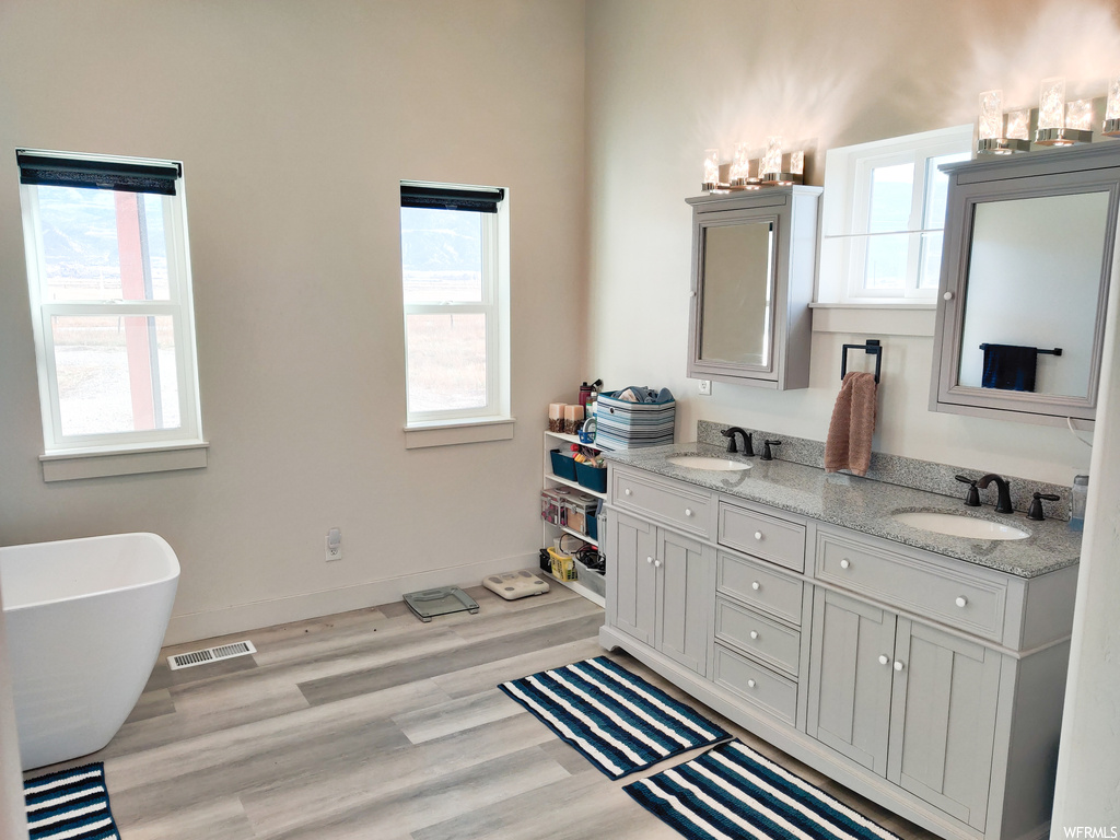 Bathroom featuring double vanity, hardwood / wood-style floors, and a bath to relax in