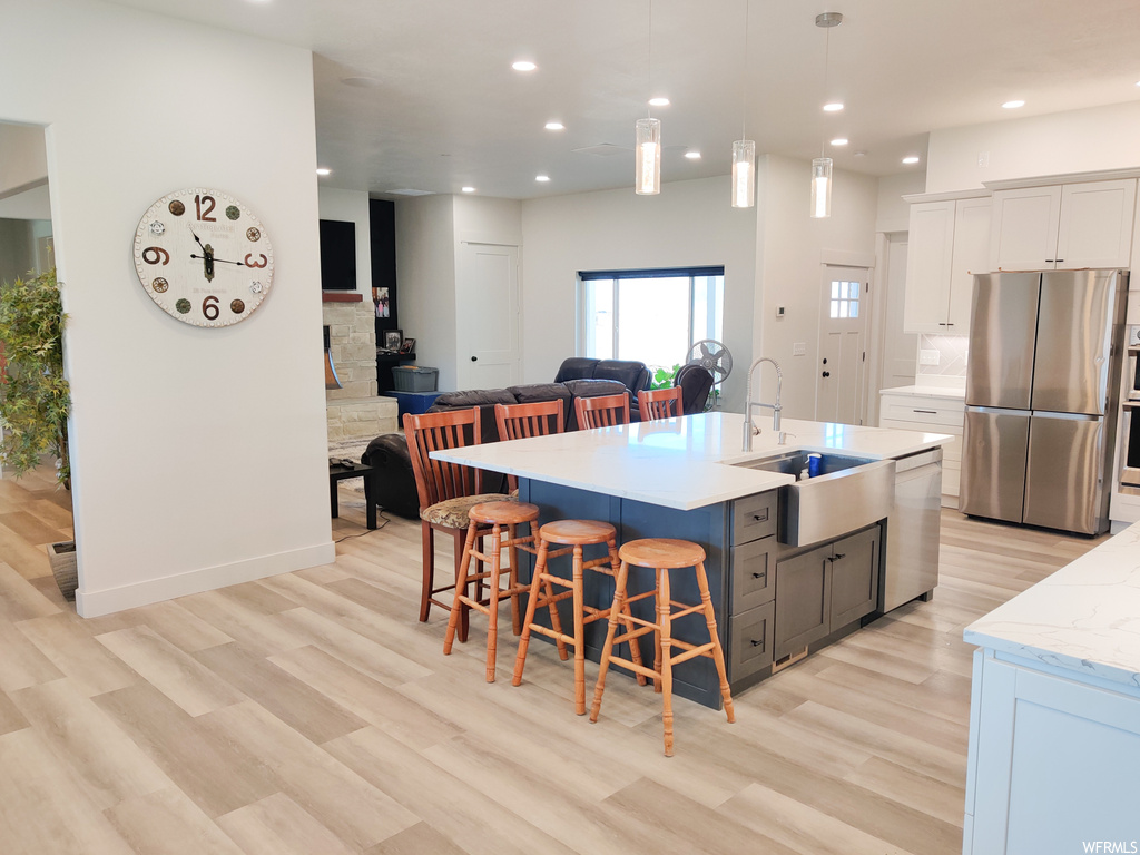 Kitchen with white cabinets, light wood-type flooring, stainless steel fridge, and dishwasher