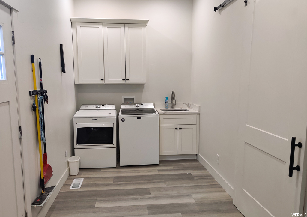 Laundry room with washing machine and clothes dryer, cabinets, sink, and light hardwood / wood-style floors