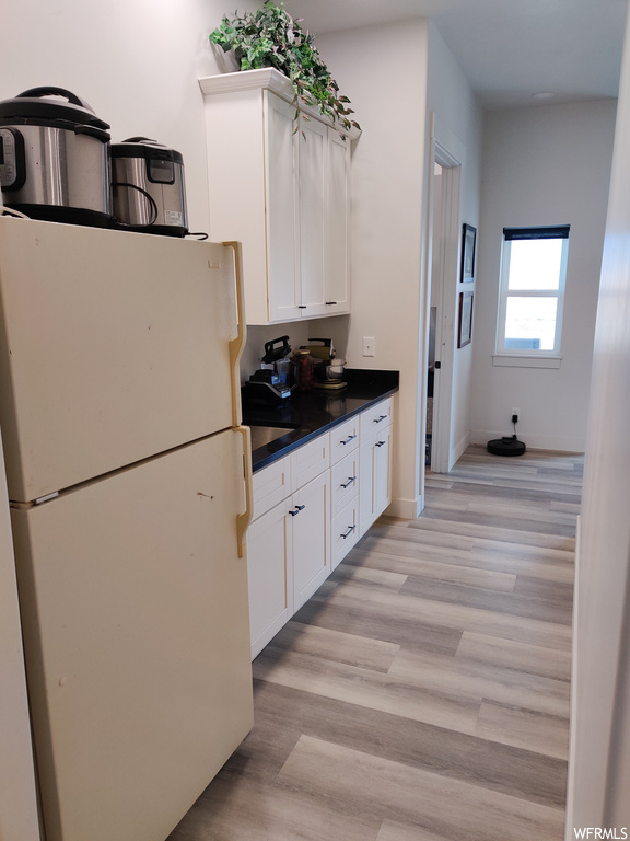 Kitchen with white cabinets, light hardwood / wood-style floors, and white fridge