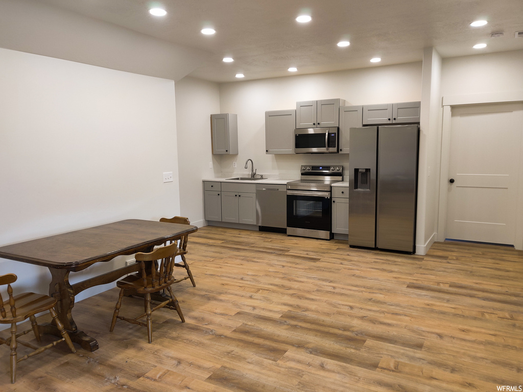 Kitchen with sink, light hardwood / wood-style floors, gray cabinets, and appliances with stainless steel finishes