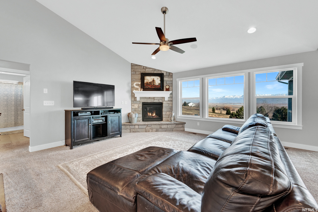 Living room featuring ceiling fan, light carpet, vaulted ceiling, and a stone fireplace