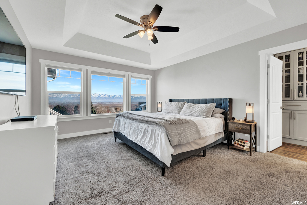 Bedroom with ceiling fan, a tray ceiling, light colored carpet, and ensuite bath