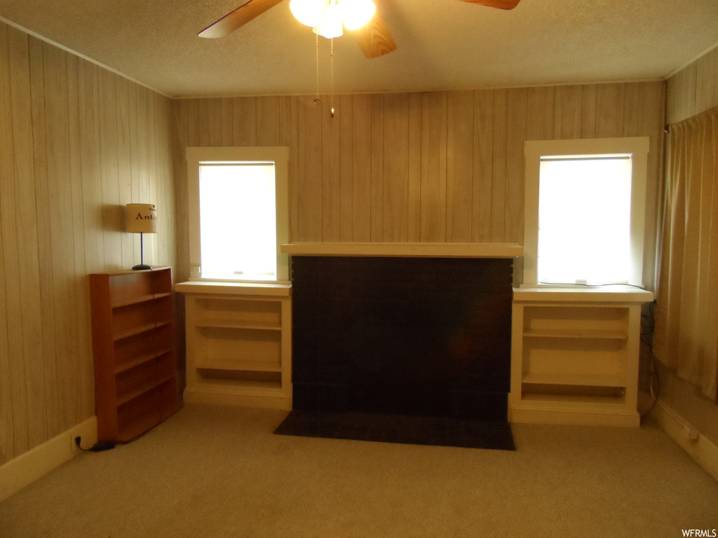 Unfurnished bedroom featuring light colored carpet, ceiling fan, wood walls, and multiple windows