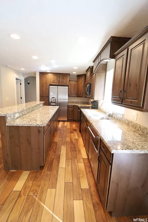 Kitchen with sink, light stone countertops, light hardwood / wood-style floors, stainless steel appliances, and a kitchen island