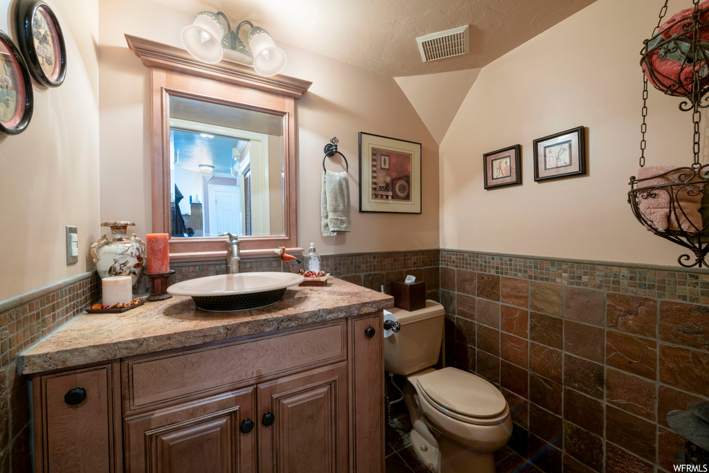 Bathroom featuring toilet, lofted ceiling, tile walls, and oversized vanity