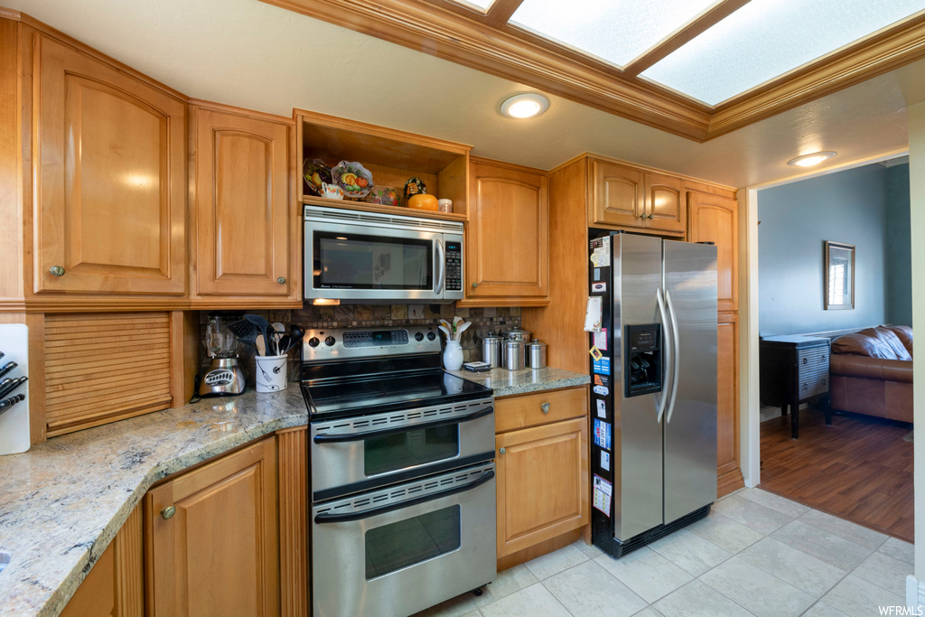 Kitchen featuring light stone countertops, tasteful backsplash, stainless steel appliances, and light tile floors