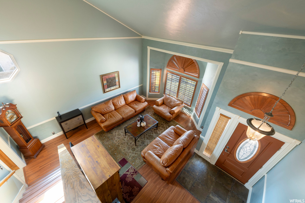 Living room featuring high vaulted ceiling, wood-type flooring, and crown molding