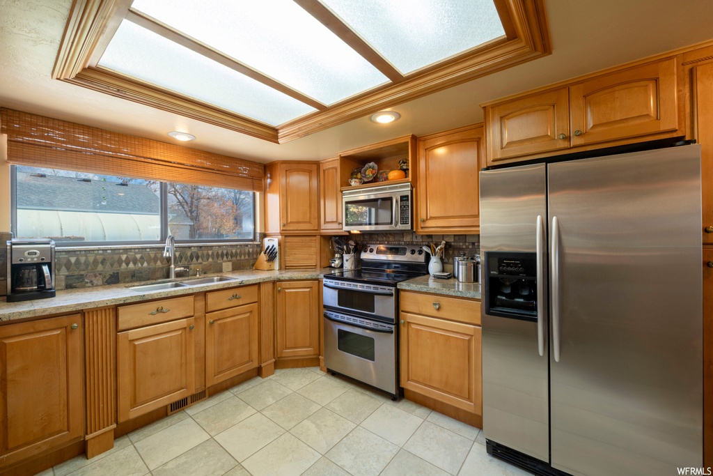 Kitchen featuring sink, appliances with stainless steel finishes, light stone countertops, a tray ceiling, and backsplash