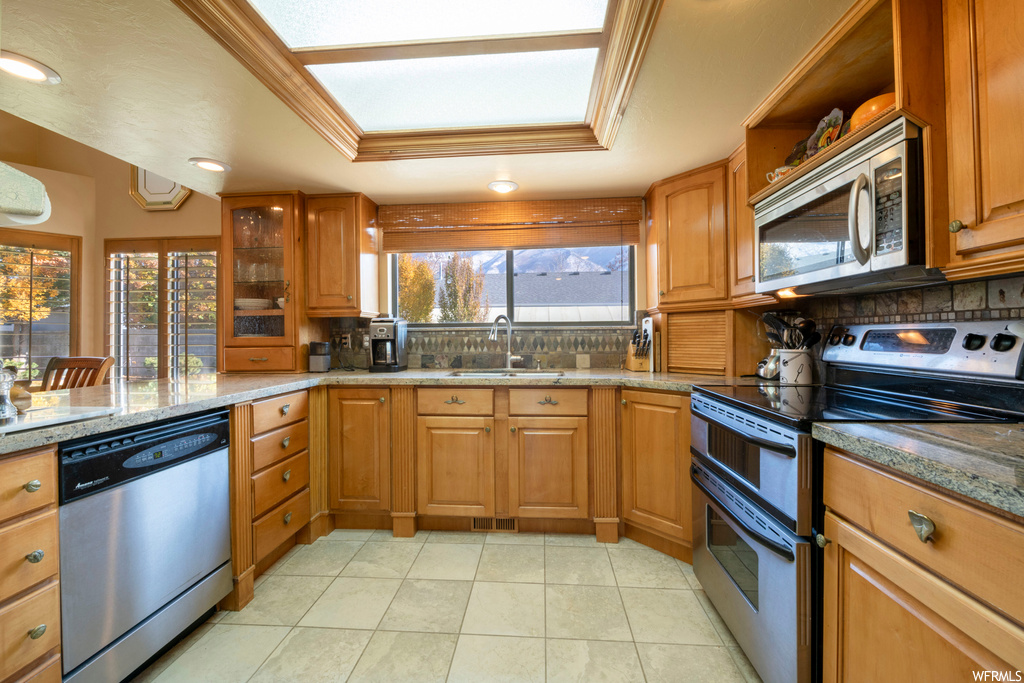 Kitchen featuring sink, tasteful backsplash, stainless steel appliances, ornamental molding, and a raised ceiling