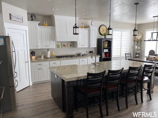 Kitchen featuring white cabinets, a breakfast bar, an island with sink, and pendant lighting